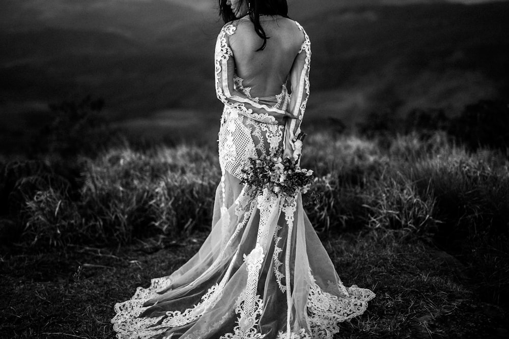 grayscale photo of woman wearing wedding dress holding bouquet of flower