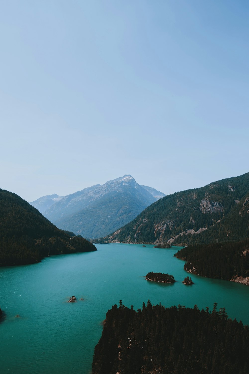 body of water between green and brown mountain range under clear blue sky during daytime