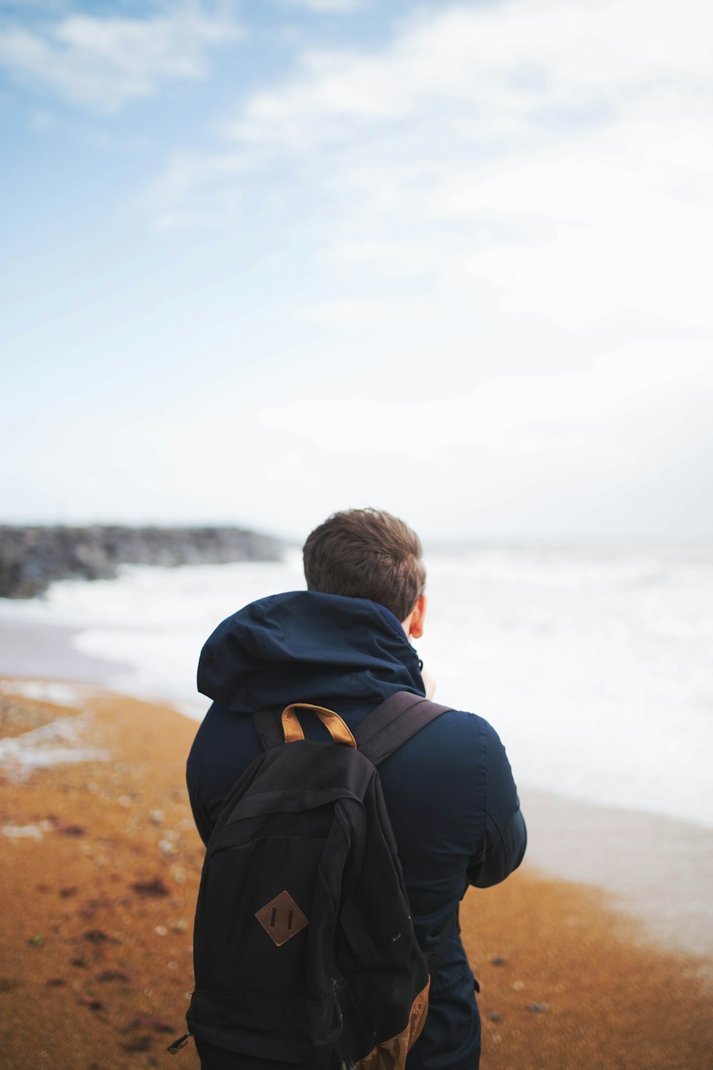 man wearing blue hooded jacket standing near the sea