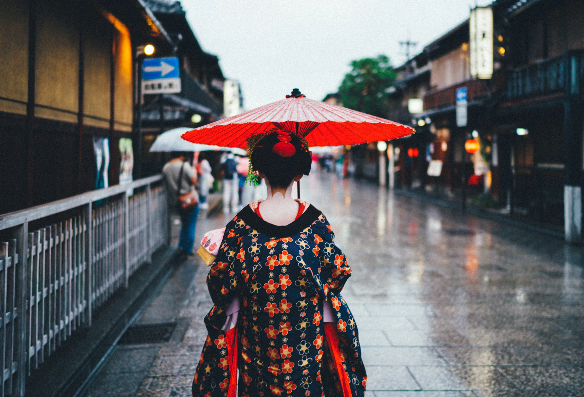 雨上がりの石畳の路地を、赤い和傘を差して歩く舞妓さんの後ろ姿