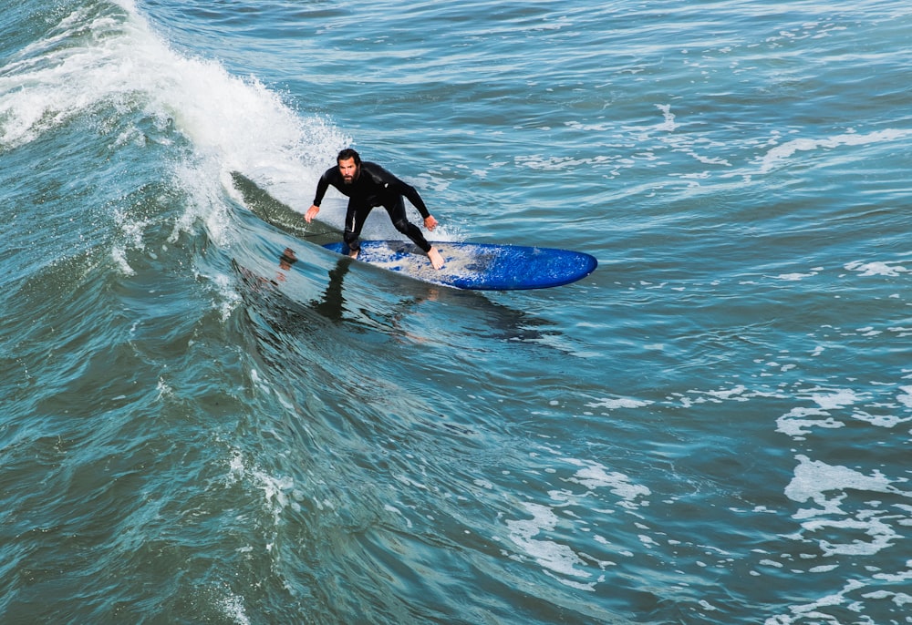 homem em roupa de mergulho preta surfando na onda durante o dia