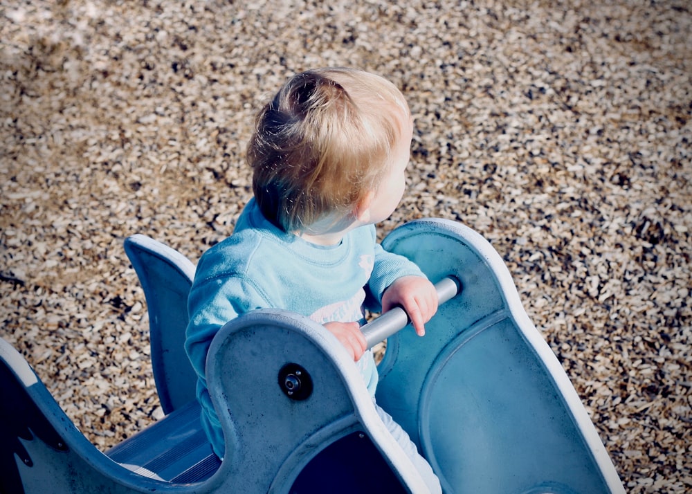 toddler sitting on blue ride during daytime