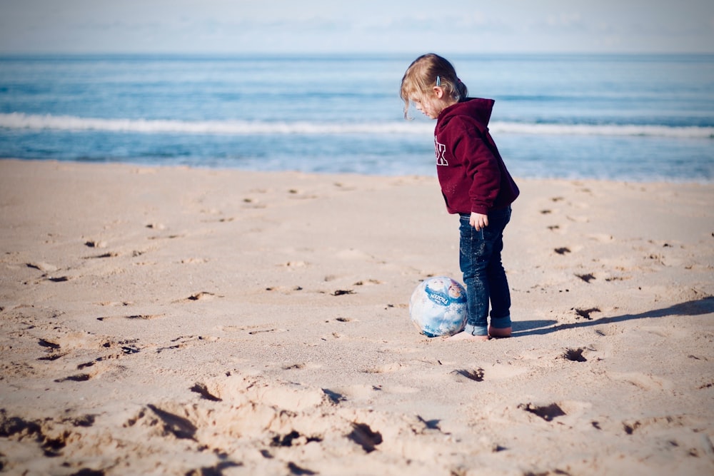 muchacha de pie al lado de la pelota en la orilla del mar