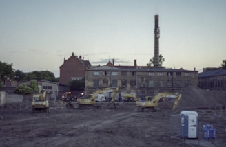 Construction workers operating heavy machinery at an urban development site during sunset.