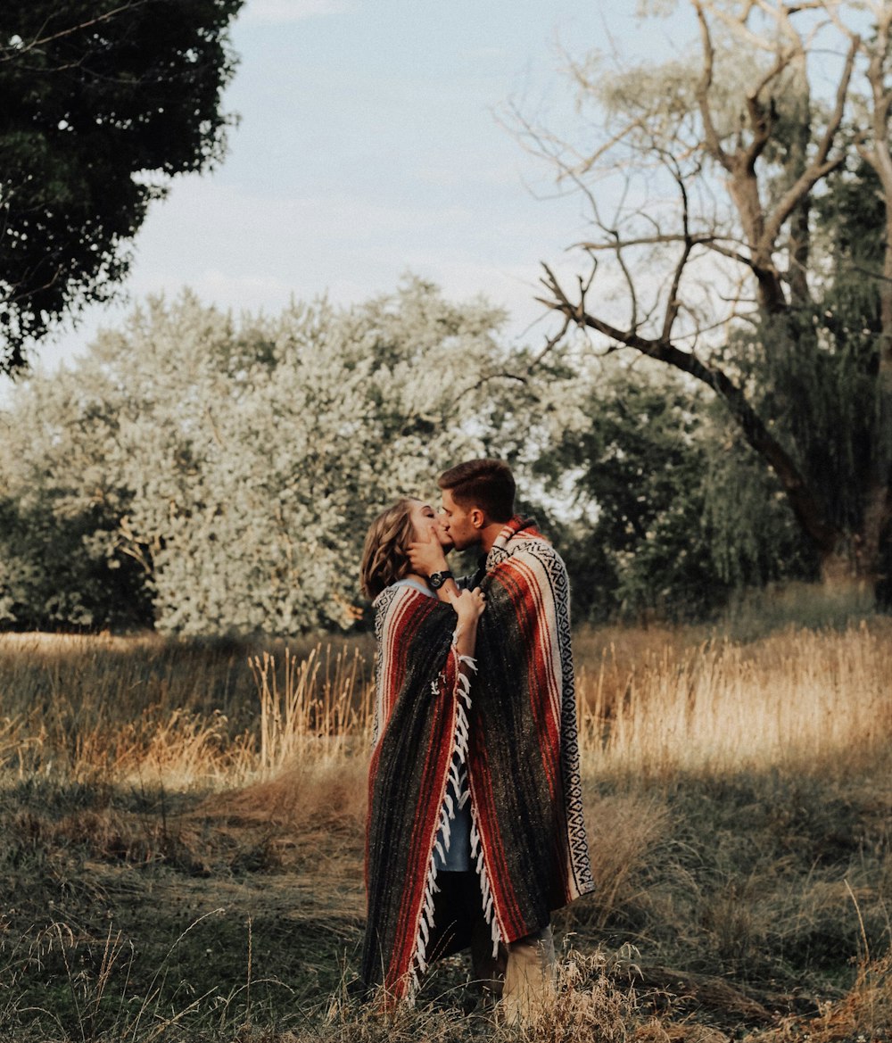 photo of man and woman kissing near brown bare tree