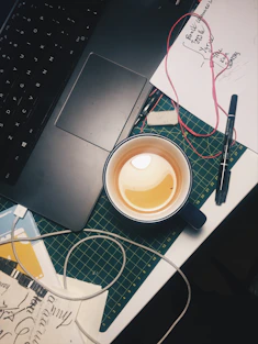 A cozy workspace with sketches, a laptop showing design drafts, and a cup of chai, capturing the creative vibe behind jacktown's storytelling and merchandise.
