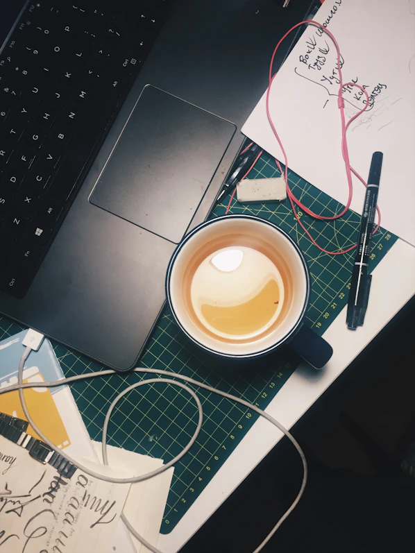 A cozy workspace with sketches, a laptop showing design drafts, and a cup of chai, capturing the creative vibe behind jacktown's storytelling and merchandise.