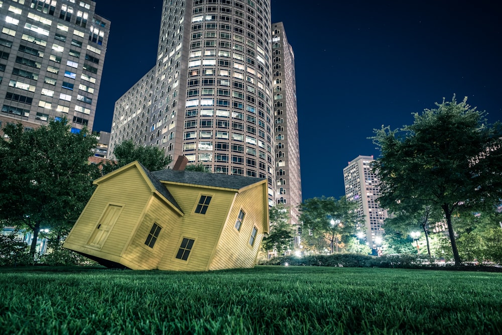 Casa gialla sull'erba verde che domina gli edifici di notte