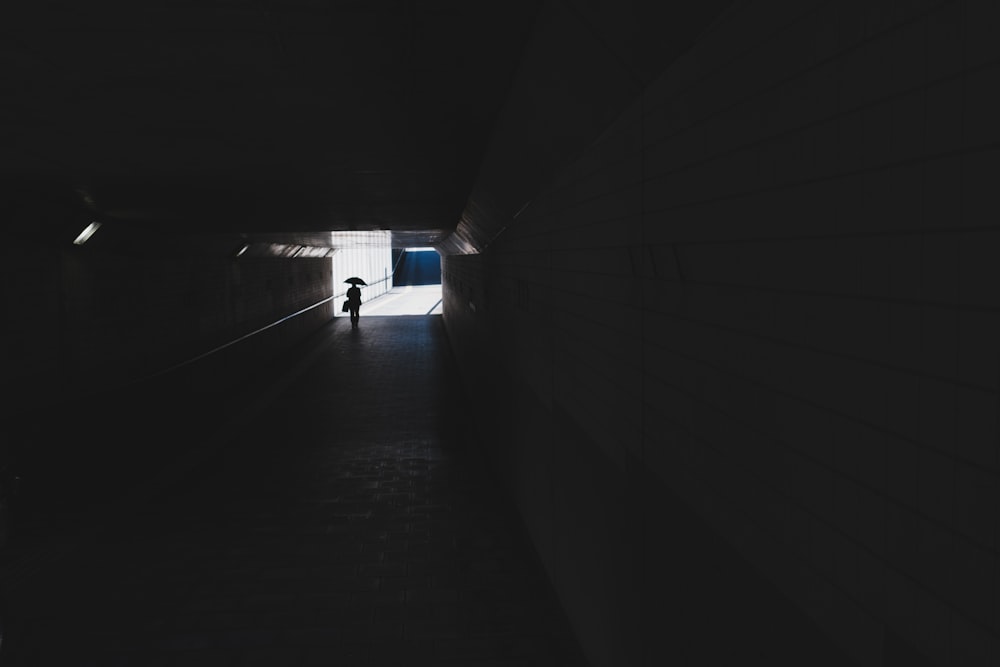 silhouette photo of person walking in tunnel