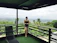 Smiling woman relaxing on a sunlit balcony overlooking lush greenery.