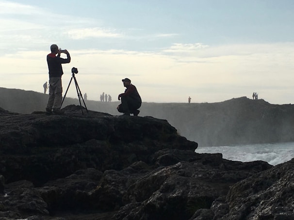 A behind-the-scenes glimpse of the videographer setting up a camera on a rocky coastline.