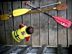 A friendly instructor helping a child put on a life jacket by a calm lake shore.