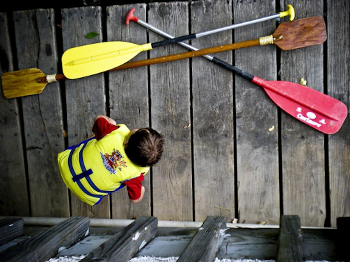 A friendly instructor helping a child put on a life jacket by a calm lake shore.