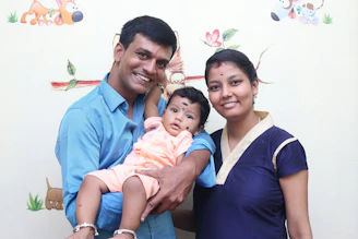 A smiling father holding his baby with a doctor in the background
