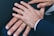 Several hands are placed together, displaying wedding rings on their fingers. The hands appear to be resting on a dark fabric surface and are wearing formal attire.