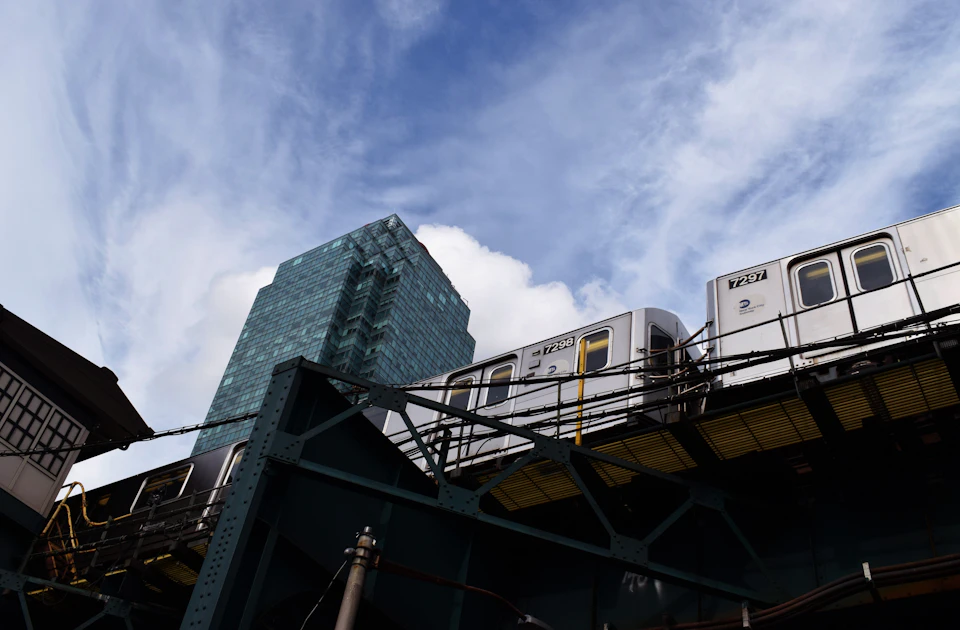 Tall glass and steel building stands against clear blue sky with fluffy white clouds nearby