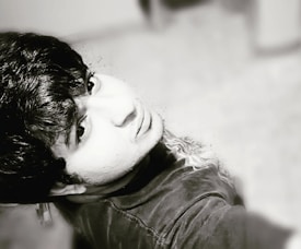 A black-and-white portrait of a person looking upwards, capturing detailed facial features and textured hair. The photo is taken at an overhead angle, emphasizing the expression and mood of the subject.