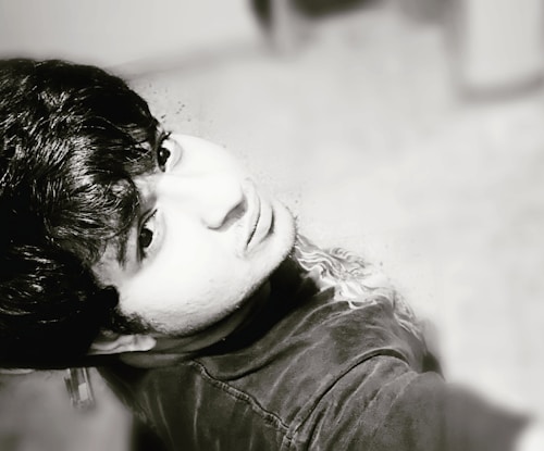 A black-and-white portrait of a person looking upwards, capturing detailed facial features and textured hair. The photo is taken at an overhead angle, emphasizing the expression and mood of the subject.