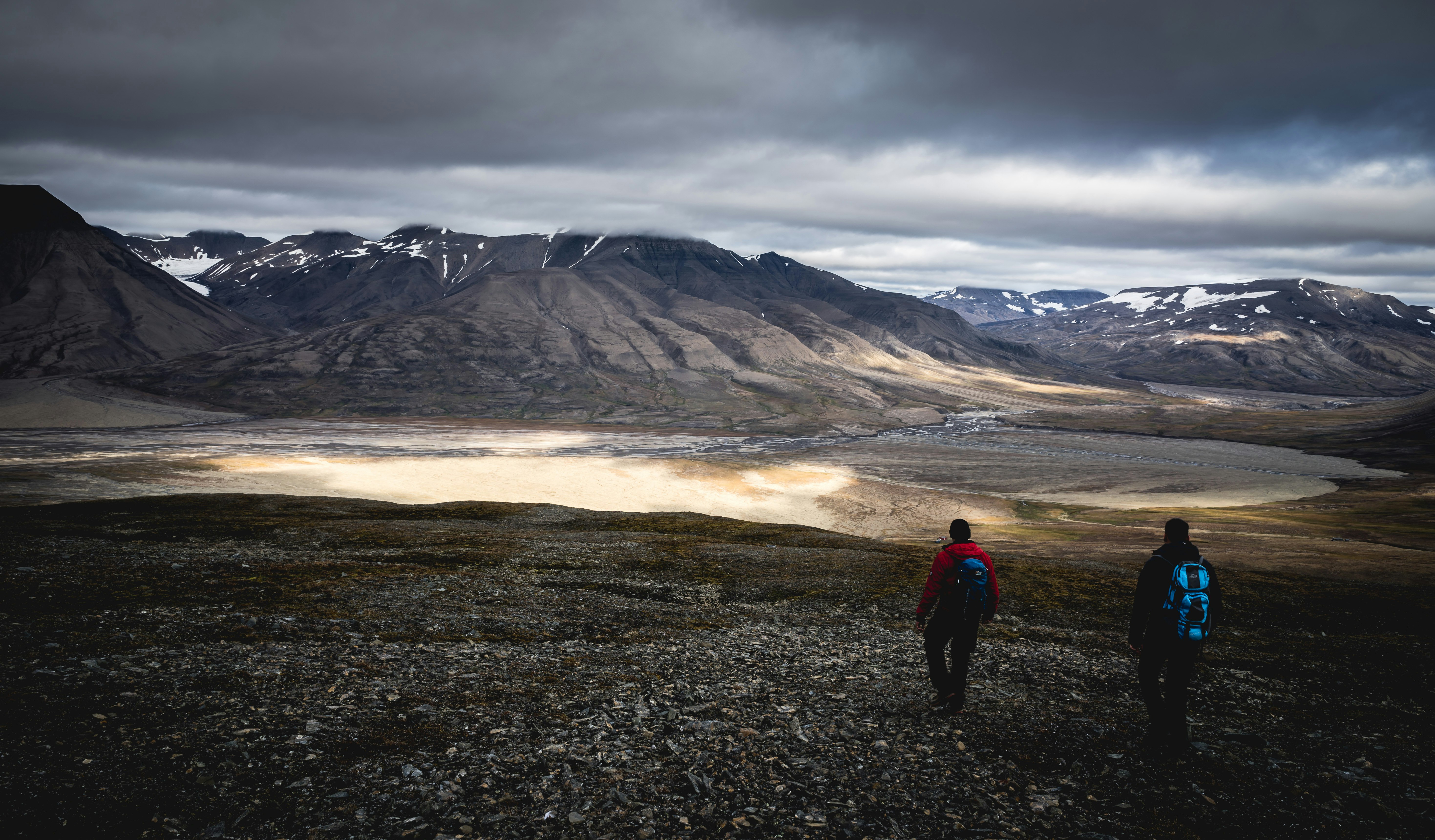 people walking across gray mountains under cloudy sky