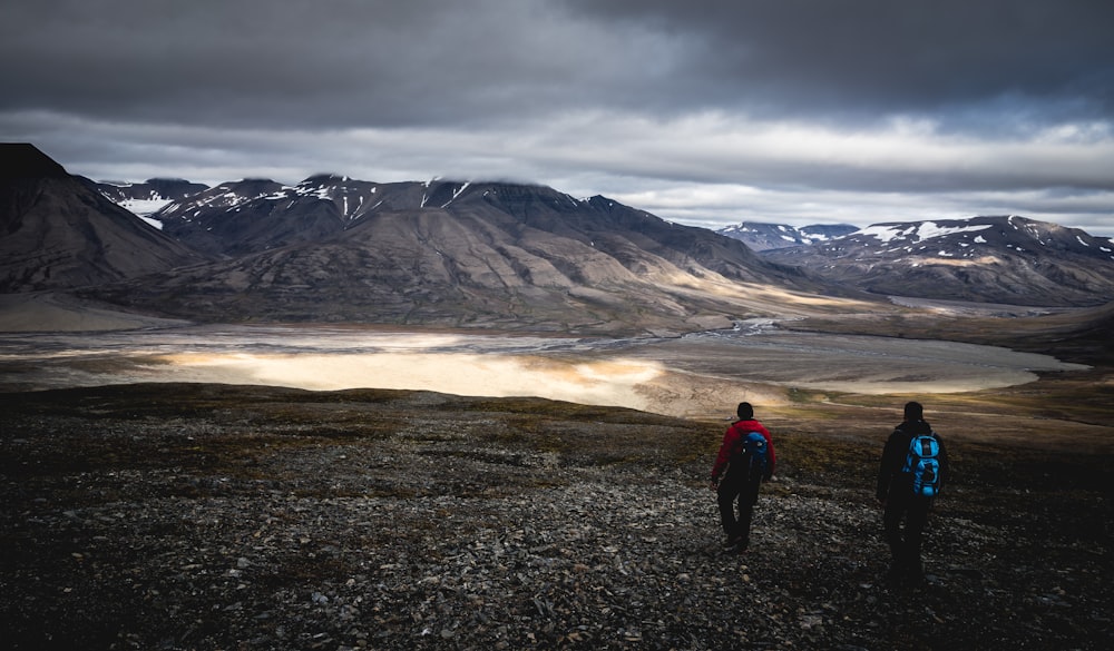 people walking across gray mountains under cloudy sky