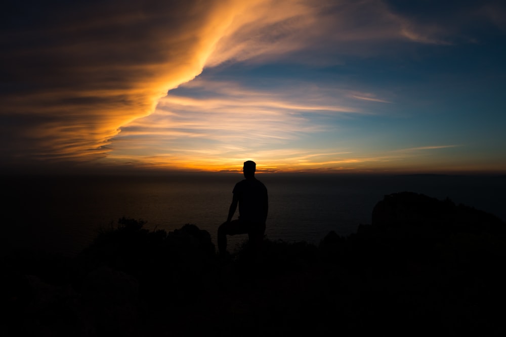 Silhouette einer Person, die zur goldenen Stunde auf einer Felsformation sitzt