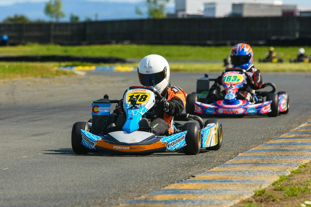 Two go-kart drivers racing on a competitive track wearing helmets and race suits