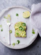 wheat bread with avocado spread beside white plastic spoon and pressed lime on round white plate