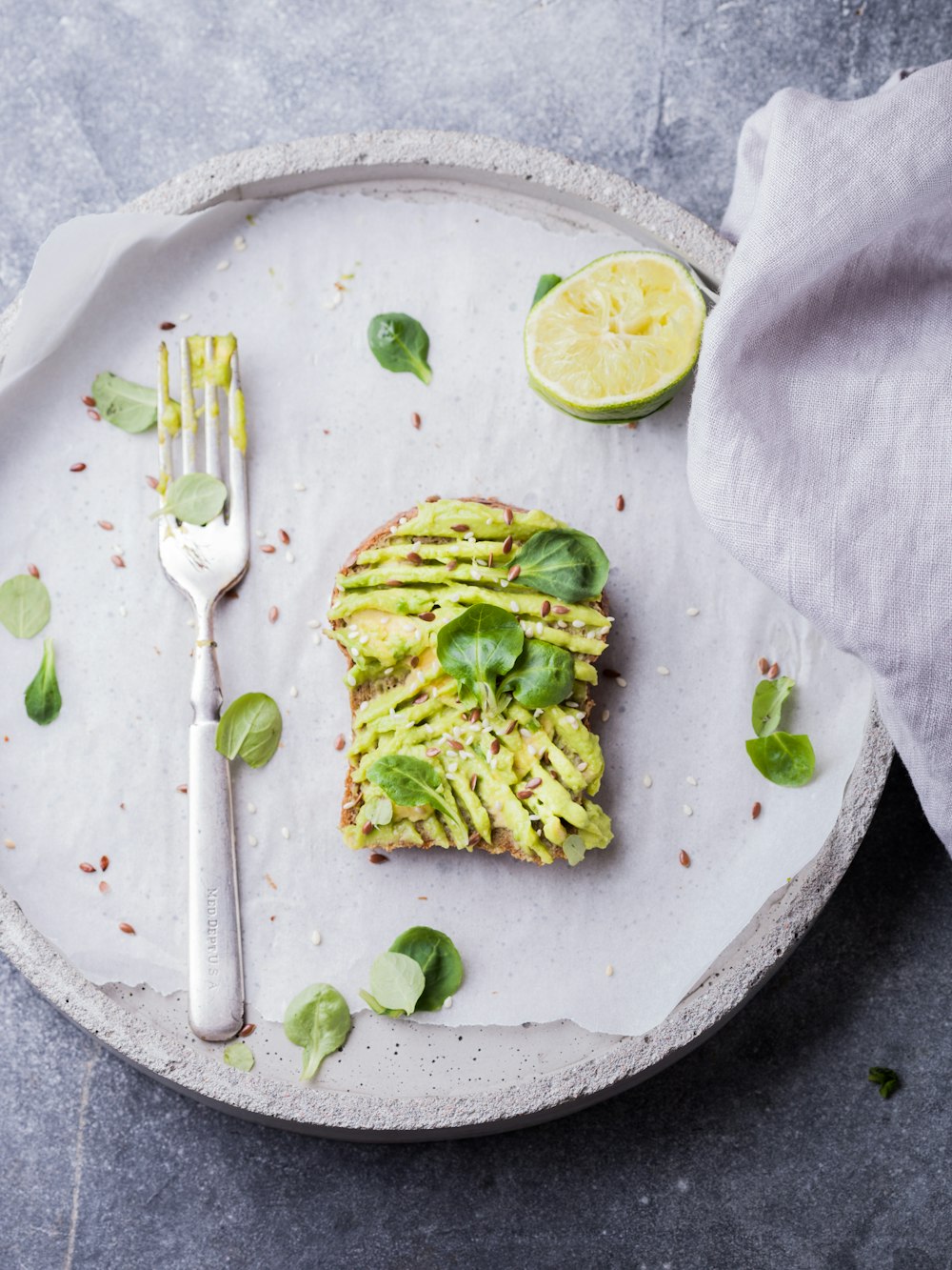 wheat bread with avocado spread beside white plastic spoon and pressed lime on round white plate