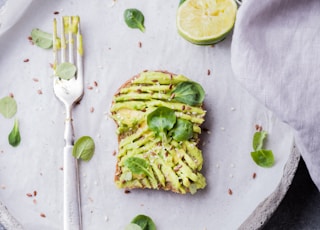 wheat bread with avocado spread beside white plastic spoon and pressed lime on round white plate