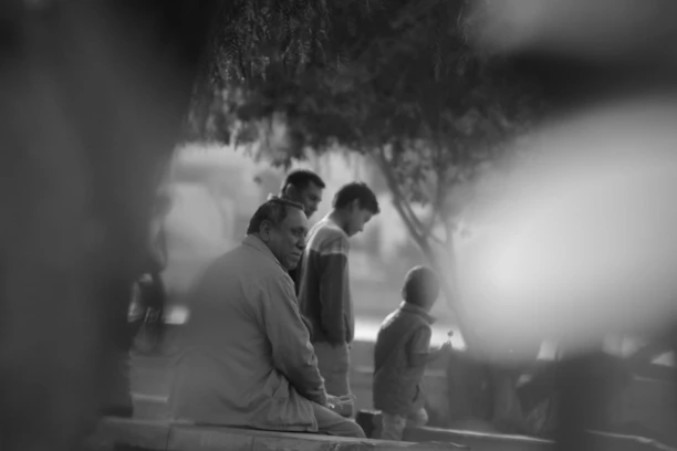 A warm, candid photo of a community mentor speaking with a group of black men in a neighborhood park.