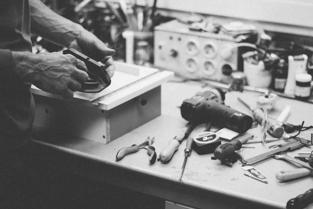 grayscale photo of person standing beside power tools on table