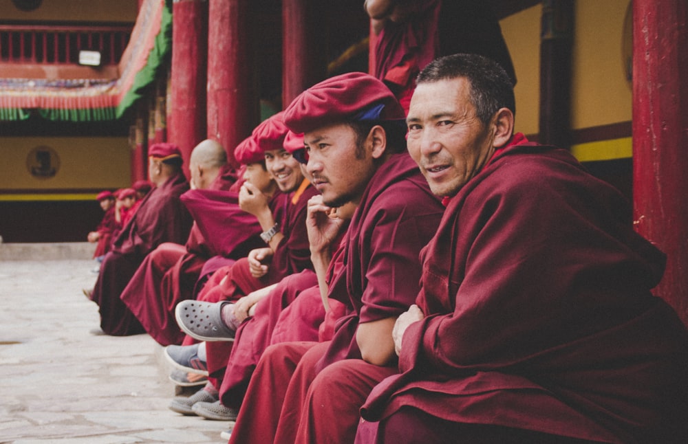 group of men wearing red dress sitting at the temple smiling while taking selfie