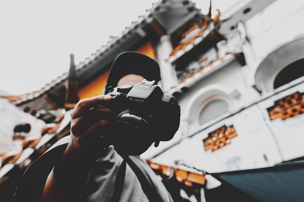 person walking near white building holding black Canon DSLR camera