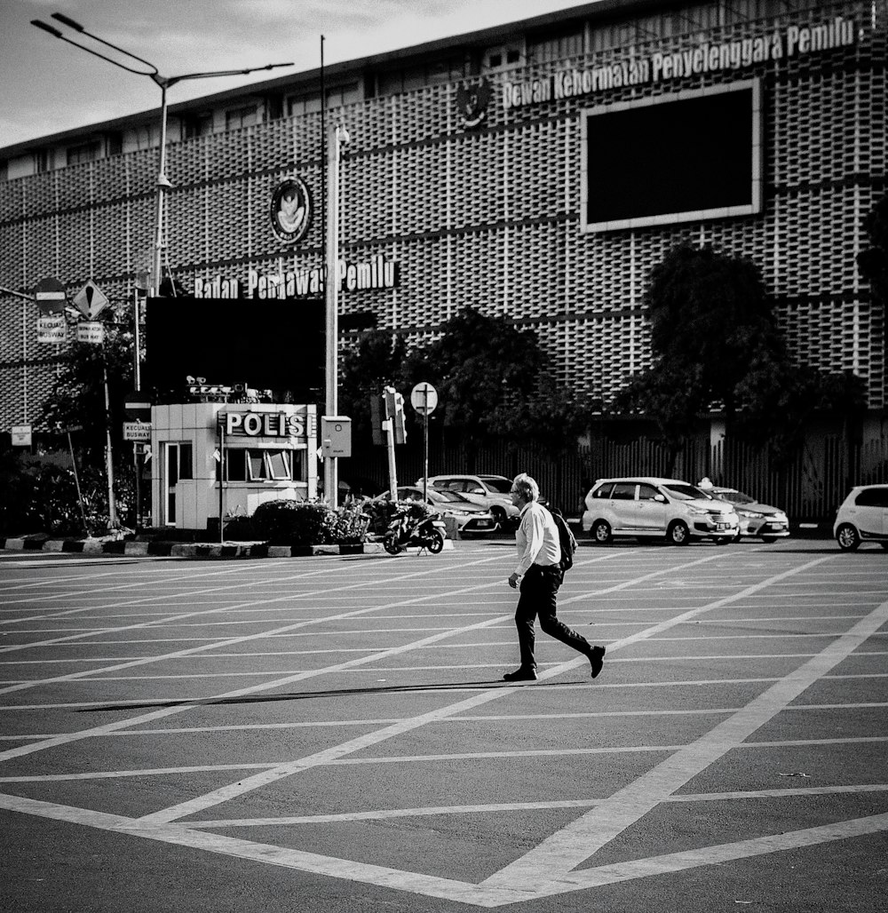 grayscale photo of man walking beside building