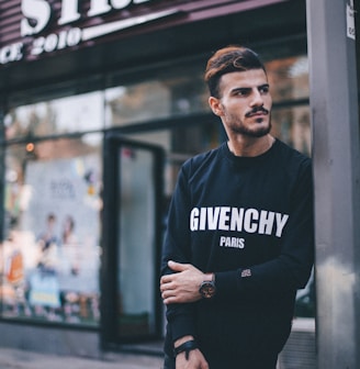 man in black Givenchy sweatshirt standing beside of post in front of Strek store during daytime shallow focus photography