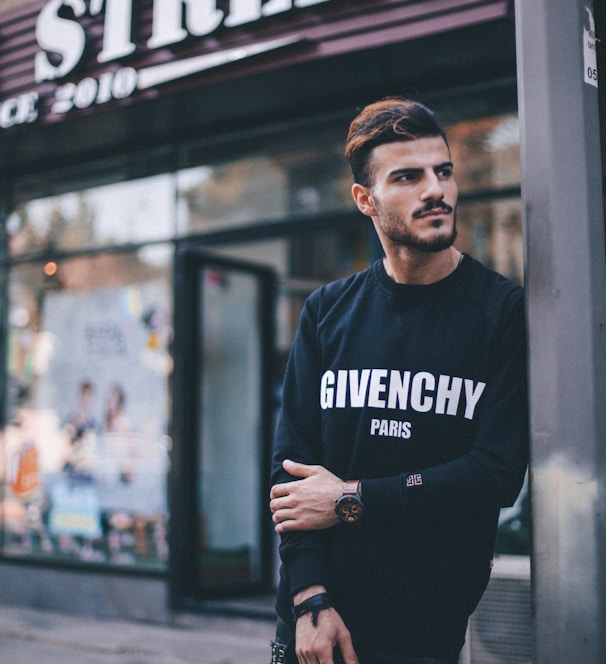 man in black Givenchy sweatshirt standing beside of post in front of Strek store during daytime shallow focus photography