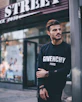 man in black Givenchy sweatshirt standing beside of post in front of Strek store during daytime shallow focus photography