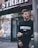 man in black Givenchy sweatshirt standing beside of post in front of Strek store during daytime shallow focus photography