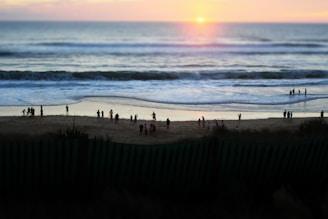 A warm gathering of community members praying together outdoors near the beach at sunset.