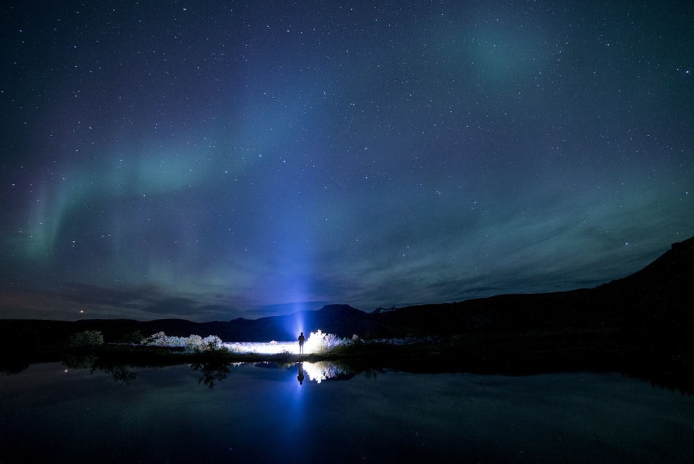 Mann, der nachts in der Nähe eines Flusses mit Aurora Borealis steht