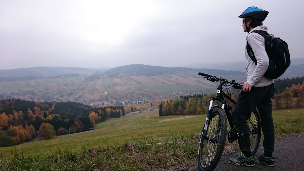 man standing on road with bicycle facing mountain range