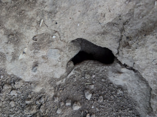 A close-up view of a rough, textured concrete surface with a significant hollow or cavity in the center surrounded by various small gravel particles and irregularities.