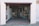 An open garage with various objects stored inside, including boxes, bottles, and shelves filled with items. A person is standing inside the garage near the back wall, partially obscured by the shadows.