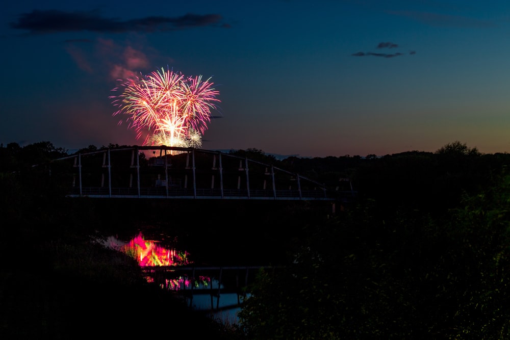 silhouette photo of suspension bridge in front of fireworks