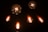 Several vintage-style incandescent light bulbs are arranged against a dark background. The bulbs emit a warm, orange glow, highlighting the intricate filament designs inside. Two large round bulbs are interspersed among four smaller teardrop-shaped bulbs.