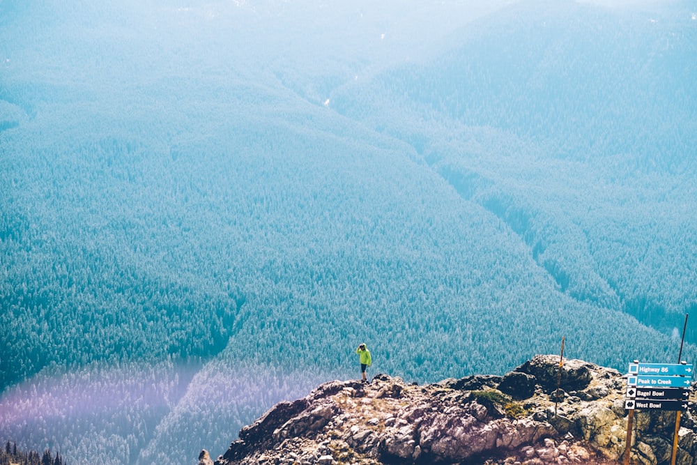 man standing on rock cliff overlooking plains at daytime