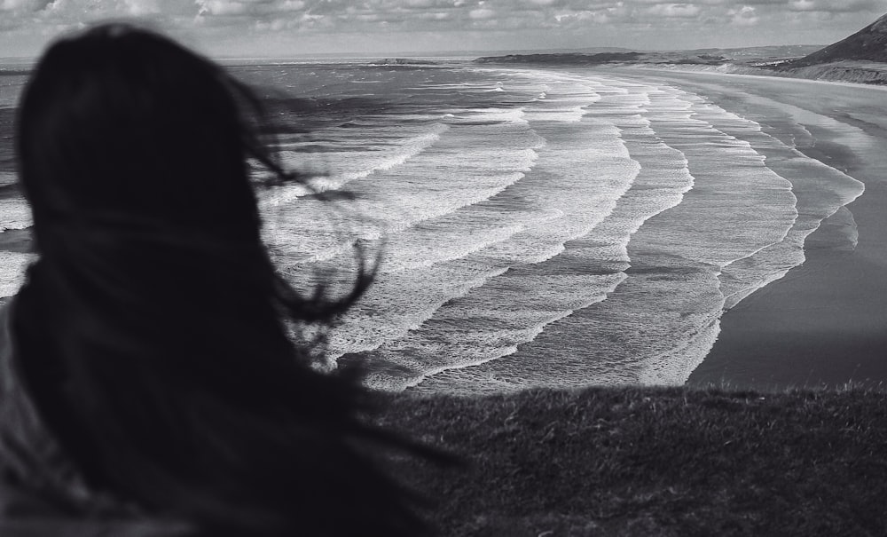 grayscale photo of woman standing near seashore