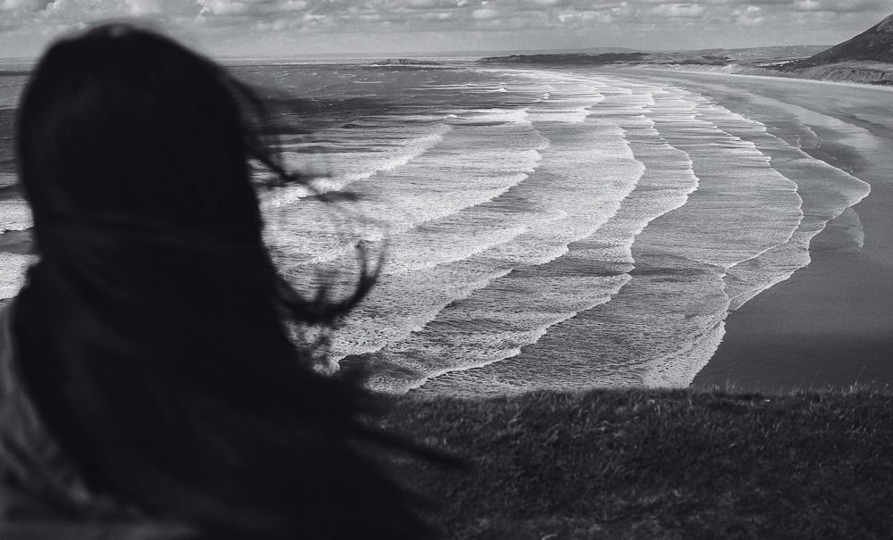 Foto en escala de grises de una mujer de pie cerca de la orilla del mar