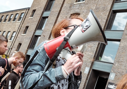 woman holding red and white megaphone standing near building