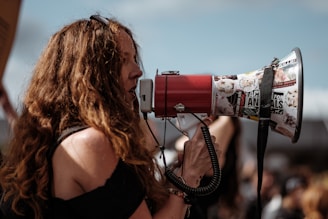 selective focus photography of woman wearing black cold-shoulder shirt using megaphone during daytime
